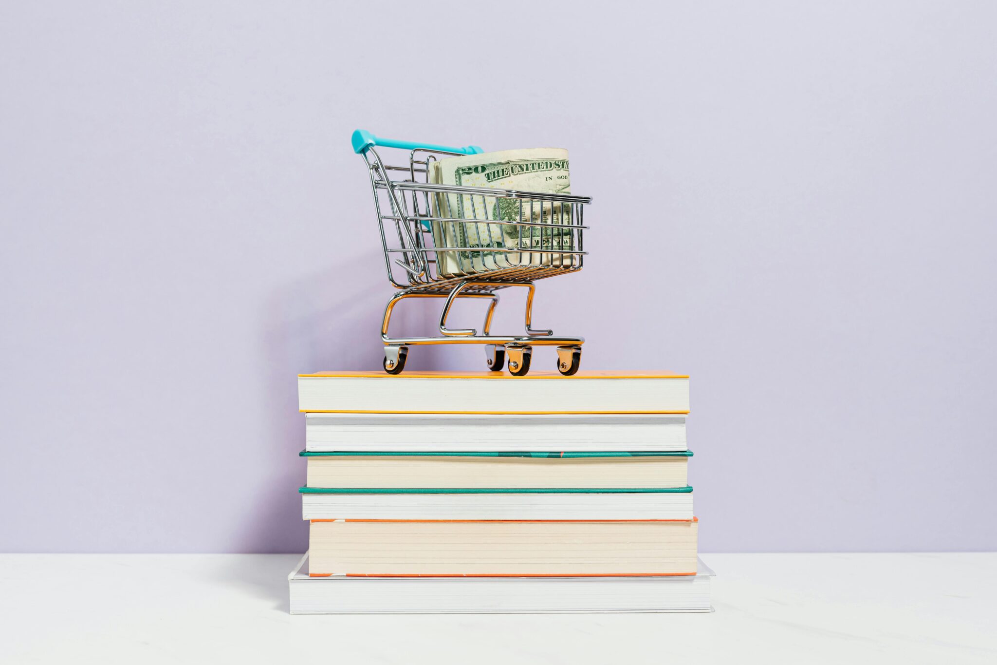 A small shopping cart with dollar bills placed on a stack of books, symbolizing financial literacy.